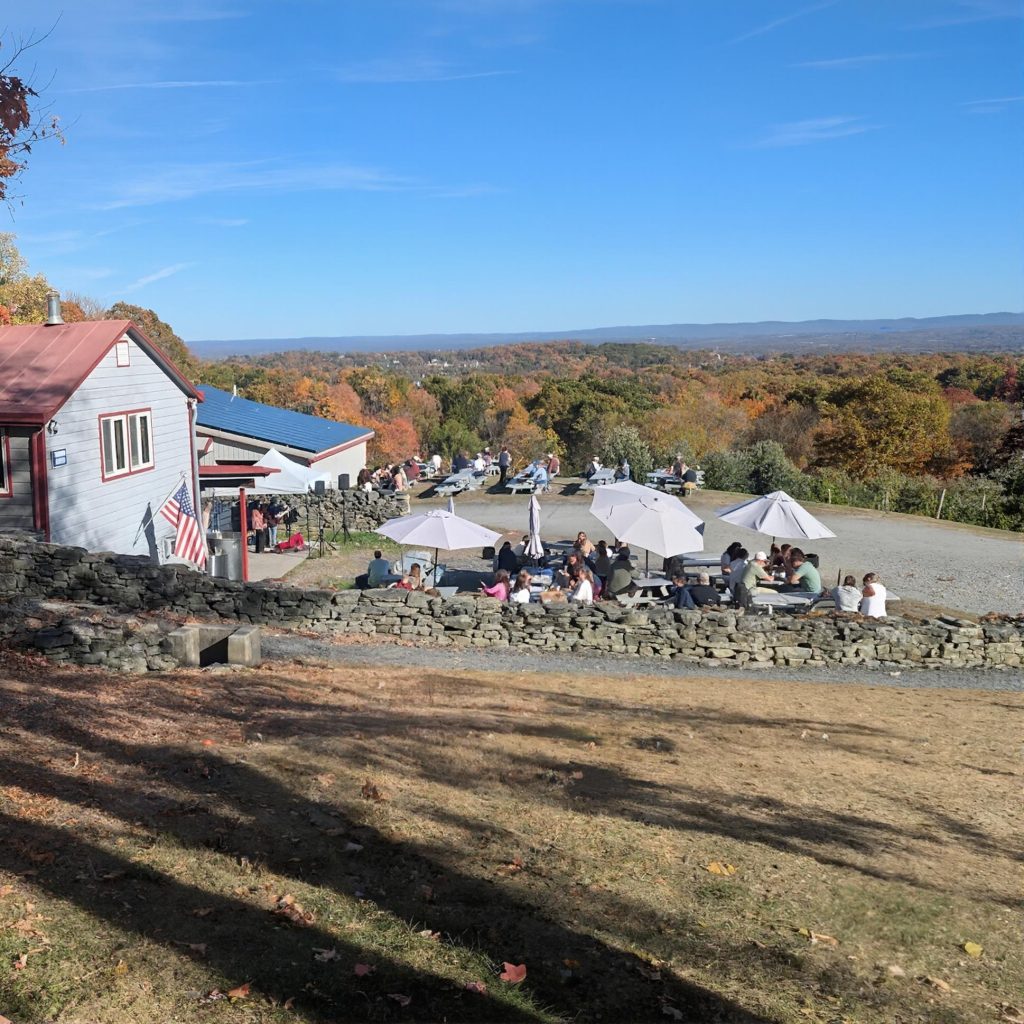 Outdoor picnic area with tables and umbrellas at Quartz Rock Vineyard in the Hudson Valley during a chauffeured wine tasting tour from Long Island.
